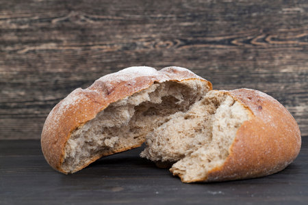 broken into half a loaf of fresh bread in black, closeup in the kitchen