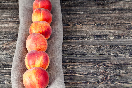 folded in a row on a linen tablecloth ripe orange peaches of a large size, lie on a wooden surface...