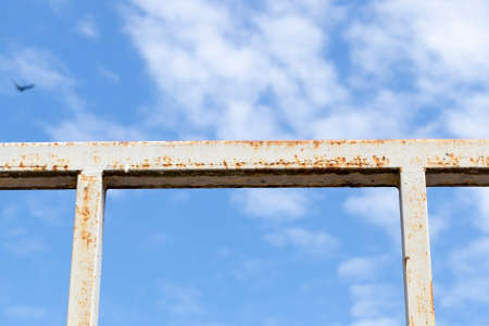 Steel metal fence with rust against the blue sky with clouds, closeupの写真素材
