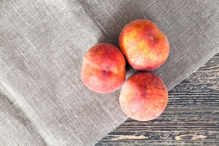 three peaches on a wooden table with a linen napkinの写真素材