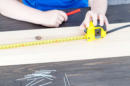 a small boy is building a wooden birdhouse, measuring the dimensions with the rulerの写真素材