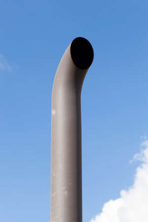 curved exhaust pipe of a tractor against the background of blue sky, dirt and soot on a metal pipeの写真素材