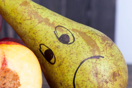 sad drawing on a pear lying near cut fruits and vegetables