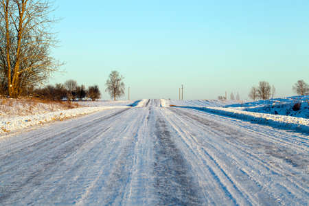 snow-covered road in the winter season. On the surface of the snowdrifts, traces of the passed cars are visible. Forest and blue sky in the backgroundの写真素材