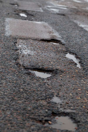 close-up photograph of a part of the highway, asphalt on which there are many pits in which rainwater is poured. Vertical frameの写真素材