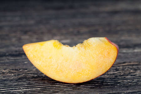 Cut off the half of a peach lying on a black wooden tableの写真素材