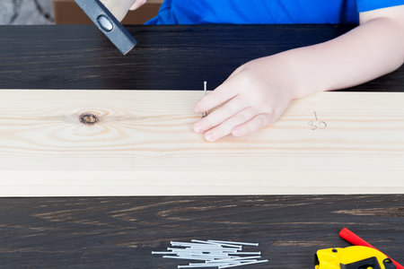 Part of a construction class where a child hammer nails into a wooden plank during a labor lesson
