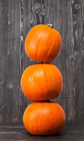 lying on top of each other Three small orange pumpkins on a wooden floor in black against a black wall of woodの写真素材