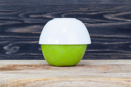 Large green apple hidden under a white porcelain or glass bowl, black kitchenの写真素材