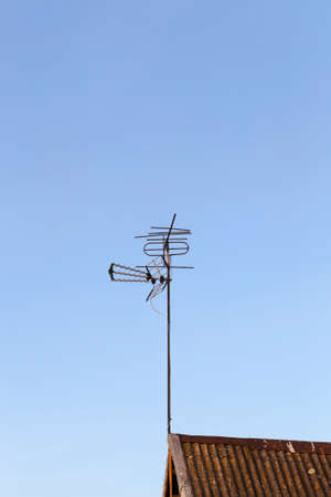 metal antenna for receiving a television signal installed on the roof of a private house, against a blue skyの写真素材