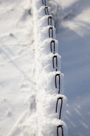 metal fence mesh covered with snow, ice and frost during the winter sunny day