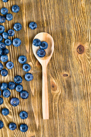 Blueberry berries on a table, summertime, photo of ripe and tasty berries scattered on a wooden table, close-up with a rustic wooden spoonの写真素材