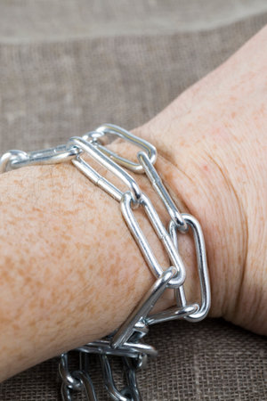 human hand tied with a strong metal chain to immobilize it close-up of a shackled human hand