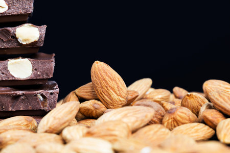 large pieces of chocolate with roasted almond kernels on a wooden table, close-up of natural cocoa...