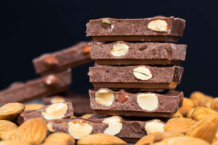 large pieces of chocolate with roasted almond kernels on a wooden table, close-up of natural cocoa products and nutsの写真素材