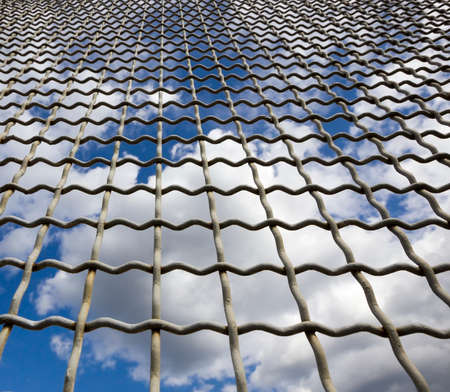 blue sky with clouds behind a metal lattice fence, Sunny weather outside the fenceの写真素材