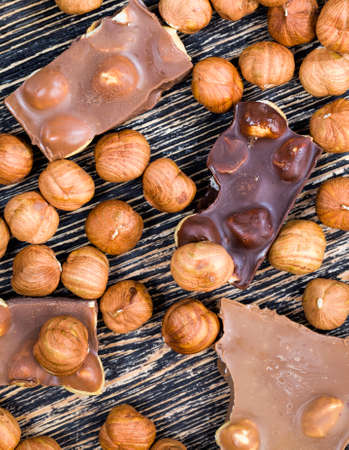 sweet milk and dark bitter chocolate , closeup with whole nuts hazelnuts in and around the broken tile chocolateの写真素材