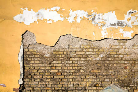 the old brick wall of the house from which part of the plaster has fallen off and destroyed, close-up of an old building during the period of its destructionの写真素材