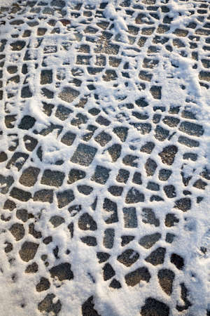 new cobblestone road covered with snow after snowfall, winter frosty weather in the cityの写真素材