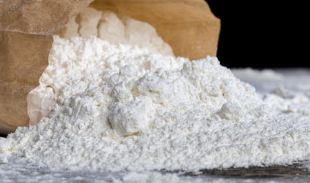 a small paper bag with durum wheat flour on the table, some of the flour powder spilled out of the...