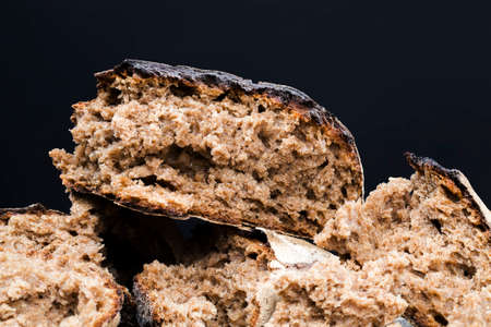 broken into pieces dark bread with a crisp crust on a wooden table, a loaf of delicious homemade bread with soft and fragrant fleshの写真素材