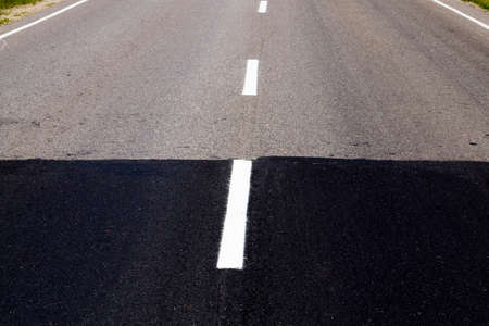 light old and black new paved road connected during the construction or reconstruction and repair of the roadway, on the asphalt is applied a line of white road markingsの写真素材