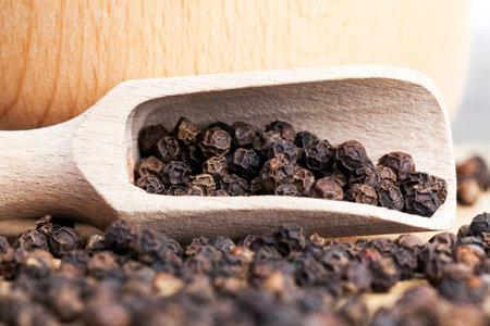black fragrant pepper with a wooden spoon, cooking with hot spices, closeup