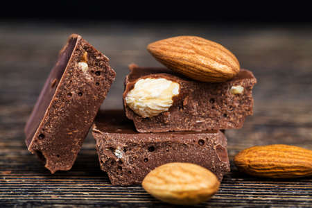 delicious roasted almonds and large pieces of chocolate on a wooden table, close-up of natural cocoa products with added sugarの写真素材