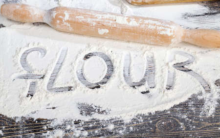 white wheat flour on a wooden table, is the ingredients for cooking durum wheat food together with a wooden rolling pin and the inscription flourの写真素材