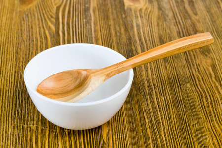 a simple wooden spoon and white glass mixing bowl on a wooden tableの写真素材