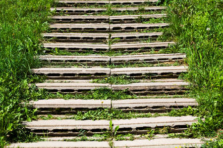 improvised stairs made of improvised materials, concrete slabs and structures with cracks and other damages, green grass grows between the slabsの写真素材