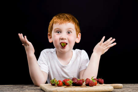 a boy eats ripe strawberriesの写真素材