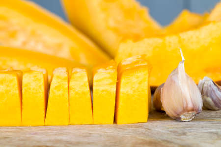 ripe orange pumpkin cut into pieces while cooking vegetarian dishes, sweet pumpkin chunks on a cutting board in the kitchenの写真素材