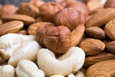 mixed together cashews, almonds and hazelnuts on a wooden table, nuts of different types together,...