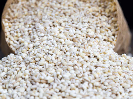 solid raw grain of pearl barley, dried grain for the production and cooking of cheap porridge, close-up of pearl barley on the kitchen tableの写真素材