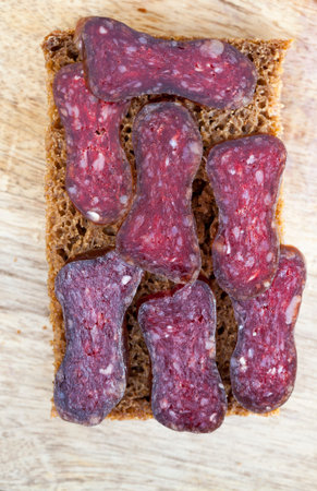 Sliced pork sausage with black rye bread on a wooden board, closeup top view