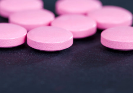Pink pills lying on a black paper background, round shape convex, for the treatment of disease