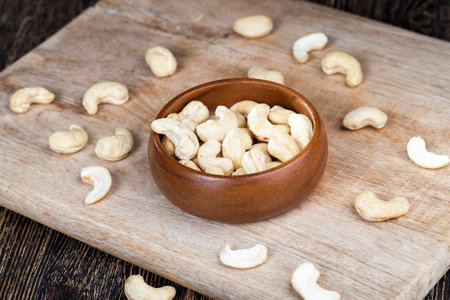 cashew nuts on an old wooden table and in a wooden bowl, close-up of a large number of cashew nuts on a table and on a wooden surface in a wooden plateの写真素材