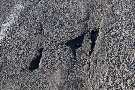 close-up of an asphalt road that needs to be reconstructed and repaired, the roadbed that becomes...