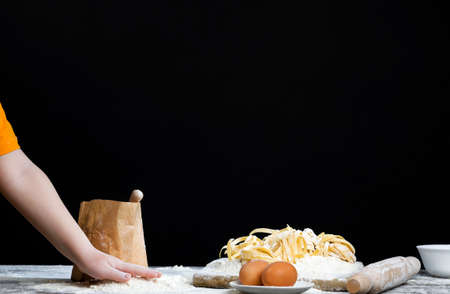 boy playing with wheat flour and other ingredients while cooking food, on kitchen table in simple kitchenの写真素材