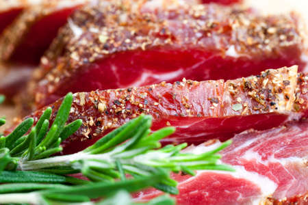 useful meat products made at the meat production plant, close-up of sliced meat with green fresh rosemary herbs and spices, dried pork meatの写真素材