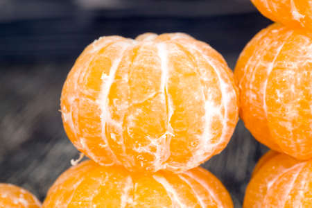 A large number of ripe peeled orange mandarins lying on a wooden table, real citrus fruits during cookingの写真素材