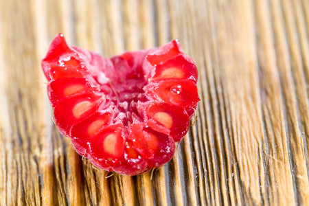 Torn half ripe berry of raspberries with small bones, close-up of the berries on the table