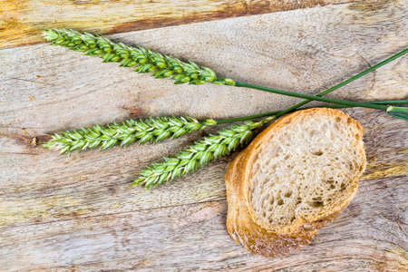 a long loaf of wheat bread cut into even pieces and pieces while cooking in the kitchen area, next to the loaf of bread are green rye spikelets on the cutting Boardの写真素材