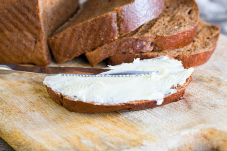fresh butter spread on pieces of a loaf of black bread baked from rye flour, close-up