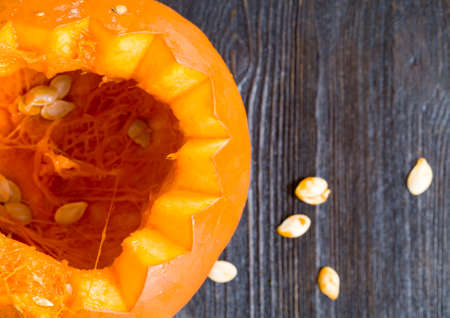 single orange pumpkin lying on a black wooden table cut for a jack lamp for halloween, close-up in the kitchenの写真素材