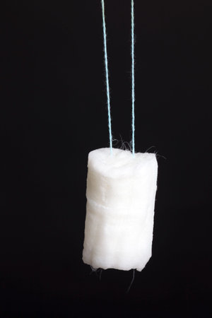 old female tampon of white color on a black background, the tampon is expanded after its immersion...