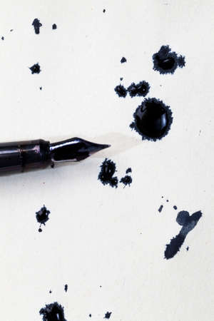 a dirty old fountain pen and black stains ink blotches on an old yellowed piece of paperの写真素材