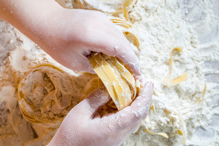 several twisted long pasta made from durum wheat flour and human baby hands, close - up of raw solid...