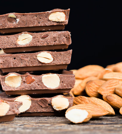 large pieces of chocolate with roasted almond kernels on a wooden table, close-up of natural cocoa...